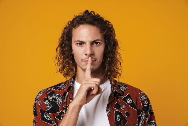 Serious young man showing silence gesture isolated over yellow background - Fotoğraf, Görsel