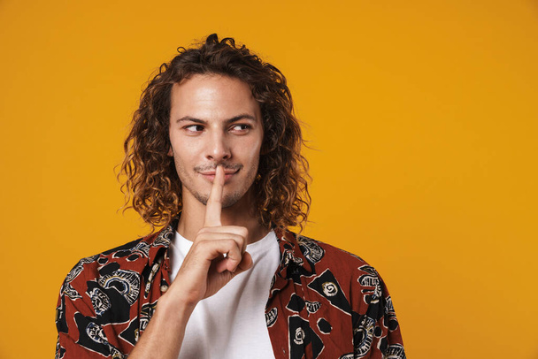 Photo of pleased handsome guy showing silence sign isolated over yellow background - Foto, imagen