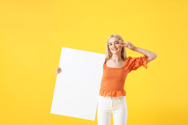 Beautiful young woman with blank poster showing victory gesture on color background - Foto, imagen