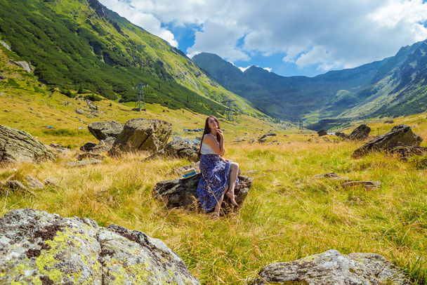 κορίτσι με μακρύ μπλε φόρεμα κάθεται σε μια πέτρα στα βουνά - Φωτογραφία, εικόνα