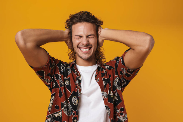Photo of irritated caucasian guy posing and covering his ears isolated over yellow background - Fotó, kép