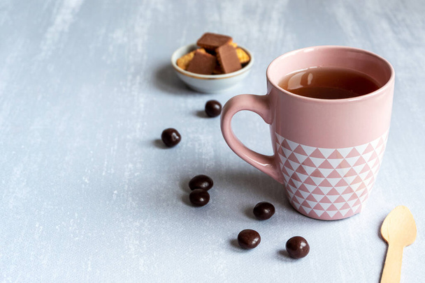 Rózsaszín csésze fekete tea szürke háttérrel, sütikkel, csokoládéval és egy fakanállal. Fénymásolási hely.  - Fotó, kép