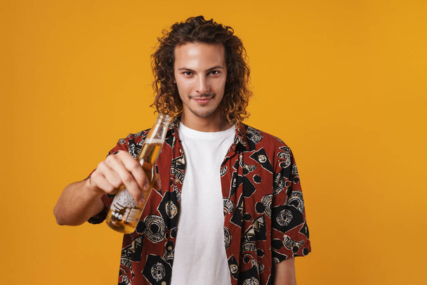 Image of cheerful young man smiling and drinking bear isolated over yellow background - Photo, image