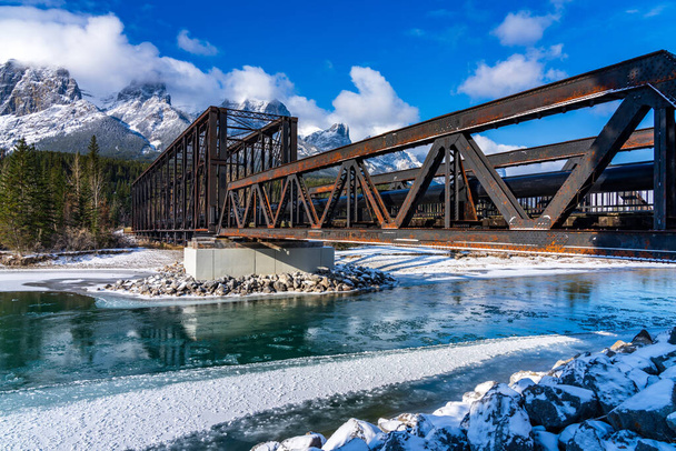 Drift ice floating on Bow River in early winter season sunny day morning. Clear blue sky, snow capped Mount Rundle mountain range in background. Landscape in Canmore Engine Bridge, Alberta, Canada. - Photo, Image