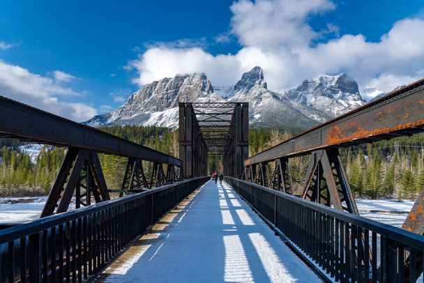 Canmore Engine Bridge in early winter season sunny day morning. Drift ice floating on Bow River. Clear blue sky, snow capped Mount Rundle mountain range in background. Landscape in Alberta, Canada. - Photo, Image