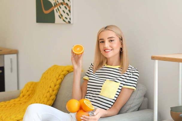 Όμορφη νεαρή γυναίκα τρώει φρέσκο πορτοκάλι στο σπίτι - Φωτογραφία, εικόνα
