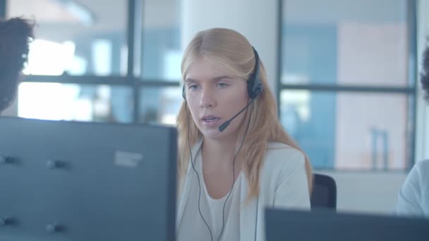 Serious young female operator in headset talking to customer - Filmati, video