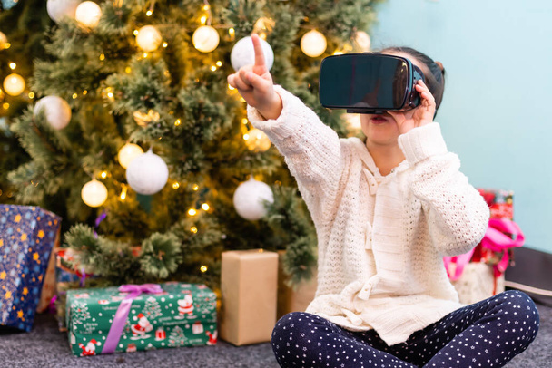 Boldog csodálkozó kislány visel virtuális valóság szemüveg néz filmeket, vagy videojátékok, elszigetelt karácsonyi háttérrel. Vidám meglepett gyermek nézett VR szemüveg és gesztikulál az ő - Fotó, kép