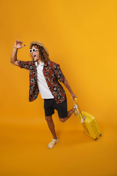 Image of excited young man in hut running with suitcase isolated over yellow wall - Foto, Imagem