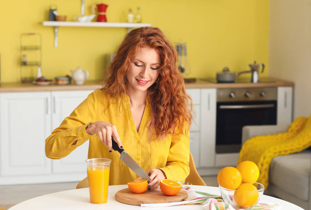 Beautiful young woman cutting fresh oranges in kitchen - Photo, Image