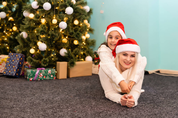 Egy fiatal és boldog anya és lánya karácsonyi kalapban. - Fotó, kép