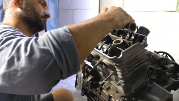 Professional mechanic repairing motor from some vehicle. Auto master fixing motorcycle engine in garage or workshop. Bearded man engaged servicing cars or motorbikes. Close up Slow motion - Footage, Video