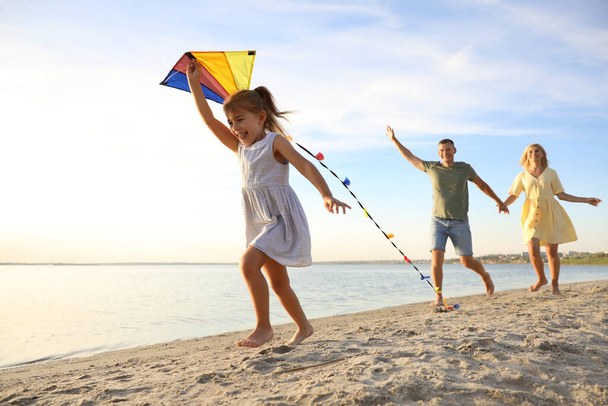 Happy parents with their child playing with kite on beach. Spending time in nature - Foto, Imagem
