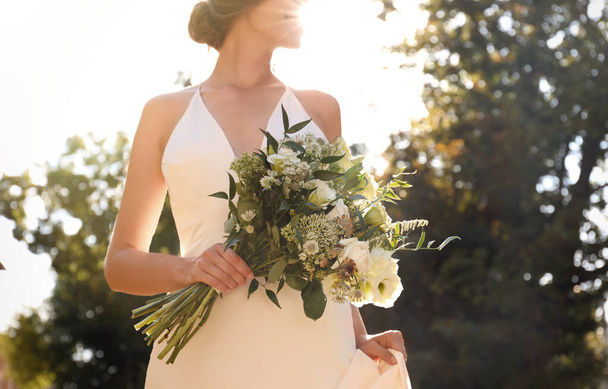 Bride in beautiful wedding dress with bouquet outdoors, closeup - Foto, Imagen