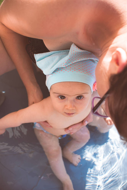 Mother holding baby girl first time in swimming pool in summer. - Photo, Image