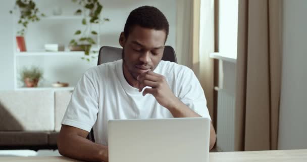 Portrait of afro american student black male tired guy wears white looks at laptop screen learns bad new feels exhaustion stress worry suffers from headache holding his head with hand, problem concept - Footage, Video