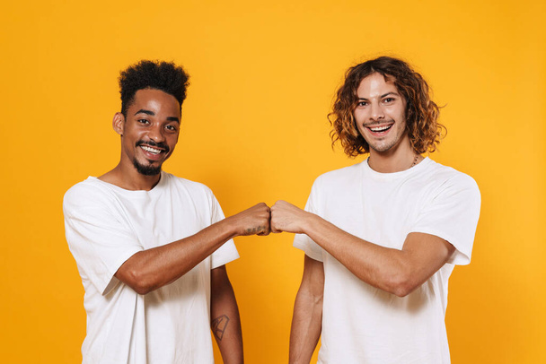 Happy multicultural two guys smiling and fist bumping isolated over yellow background - Fotografie, Obrázek