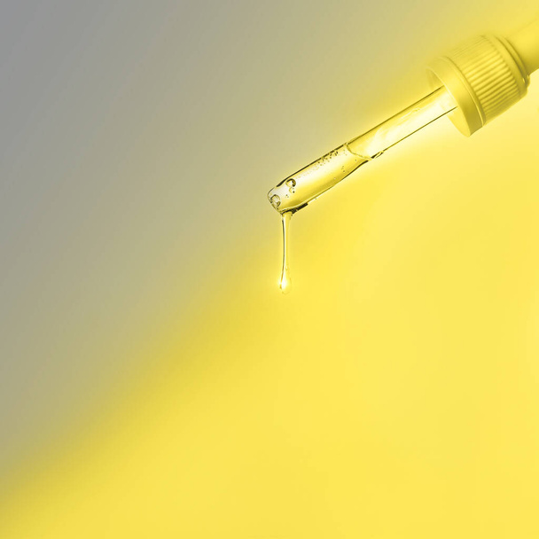 Pipette with drop of serum or hyaluronic acid on bright illuminating yellow and gray natural color background.  - Photo, Image