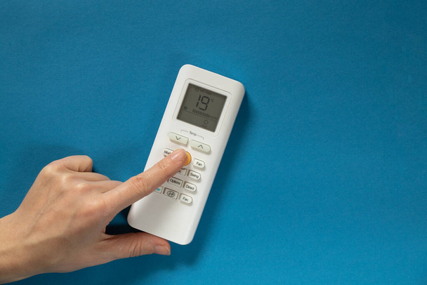 weibliche Hand schaltet Taste auf weiße Fernbedienung der Klimaanlage auf isoliertem Hintergrund - Foto, Bild