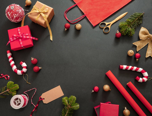 Préparation des cadeaux de Noël. Coffrets cadeaux enveloppant plat posé sur fond noir, vue de dessus. Ornements et accessoires de couleur rouge, modèle de carte, espace de copie - Photo, image