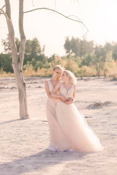 Dvě nevěsty ženy v bílých šatech s blond vlasy objímající se navzájem, lesbická svatba - Fotografie, Obrázek