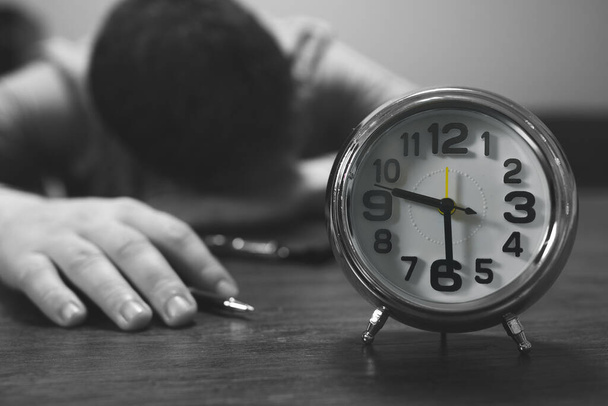 El reloj muestra las nueve y media de la noche. El hombre se durmió en el trabajo. - Foto, imagen
