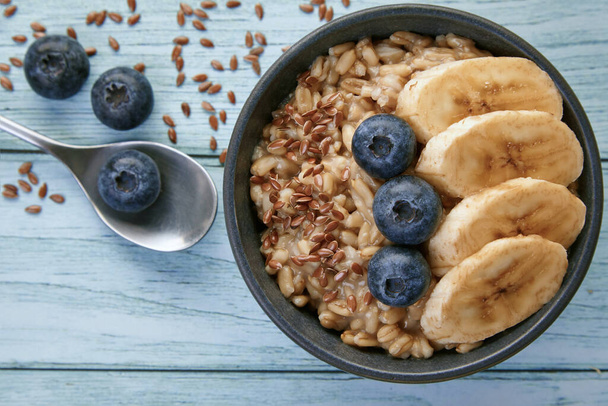 Whole grain oatmeal with blueberries and banana slices in a dark grey bowl - Foto, afbeelding