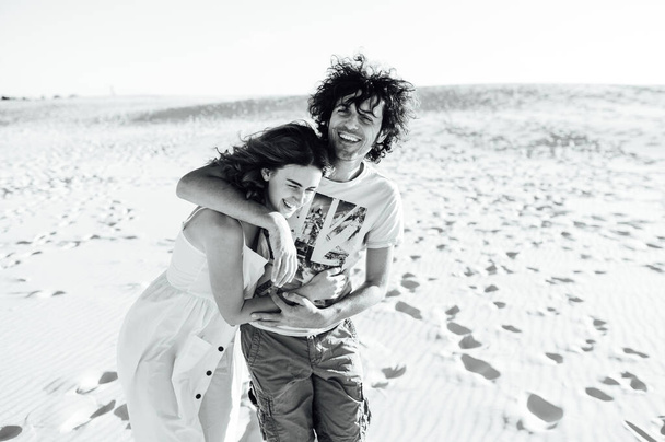 a guy with curly hair and his girlfriend are hugging cheerfully on the sand - Fotó, kép