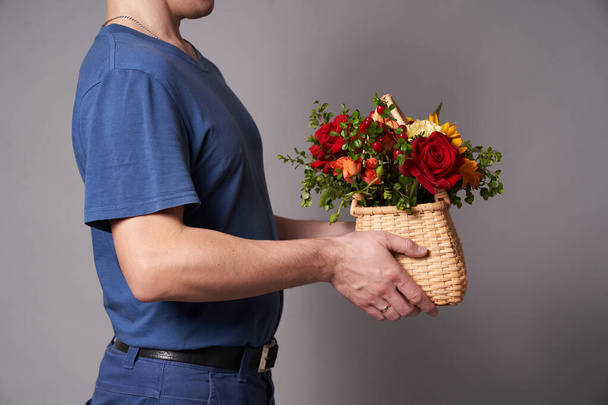 Hand of a man in a glove with basket of flowers on a gray background - Photo, Image