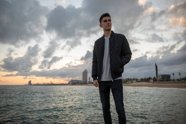 Young man wearing jacket looking sideways, city and water in background - Foto, Imagem