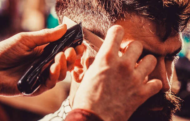 Barber works with hair clipper. Hipster client getting haircut. Hands of barber with hair clipper, close up - Photo, Image