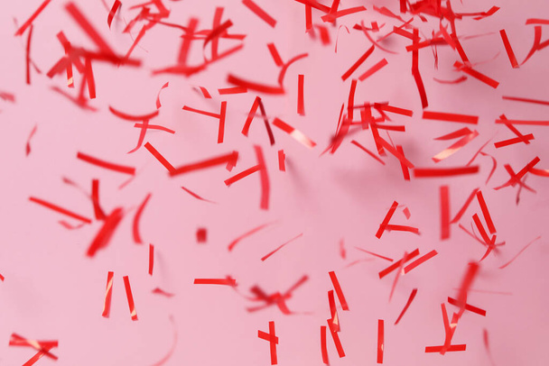 Shiny red confetti falling down on pink background - Foto, afbeelding