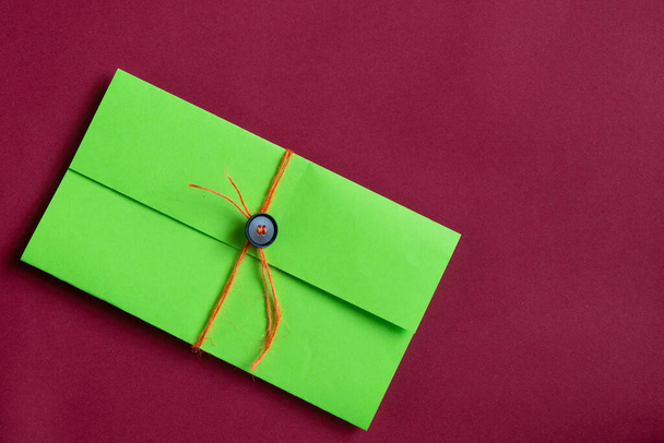 zelená domácí obálka s provazem na knoflíku na červeném pozadí, dárek - Fotografie, Obrázek