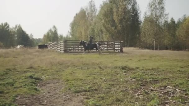 Un cavalier expérimenté montre à une femme comment contrôler un cheval alors qu'elle monte à côté d'un enclos en bois dans un club équestre de campagne. - Séquence, vidéo