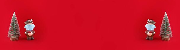 Árbol de Navidad y estatuilla de cerámica de Buey en máscara médica sobre un fondo rojo. Amplio banner con espacio de copia. Símbolo del nuevo año 2021. - Foto, Imagen