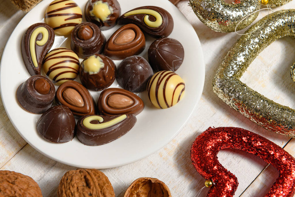 Noel ya da tatil süslemeleri için tatlı yemek arkaplanı - çikolata şekerlemeleri, mandalinalar, fındıklar ve kuru meyveler beyaz ahşap üzerinde - Fotoğraf, Görsel