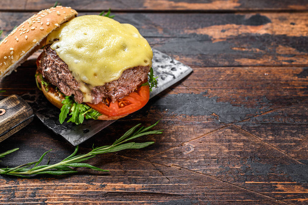 Grilled homemade burger with beef, tomato, cheese, cucumber and lettuce on a meat cleaver. Dark wooden background. Top view. Copy space. - Photo, Image