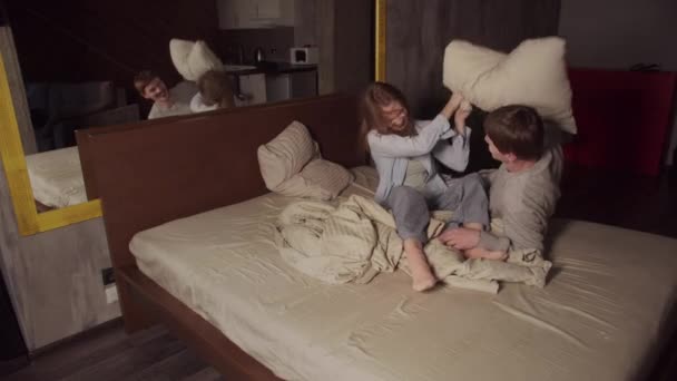 Un jeune couple marié qui s'amuse dans un grand lit dans un hôtel, ils jouent et se battent avec des oreillers. - Séquence, vidéo