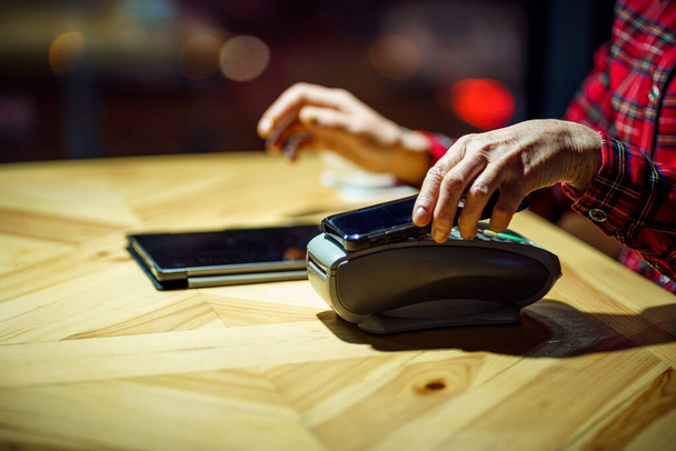 Kontaktloses Bezahlen. Nfs Zahlung per Telefon. Der Kunde eines Cafés oder Restaurants hält das Smartphone über den elektronischen Zahlungsautomaten, während er die mobile App benutzt, um zu bezahlen. Bargeldlose Zahlung. NFC-Technologie. - Foto, Bild
