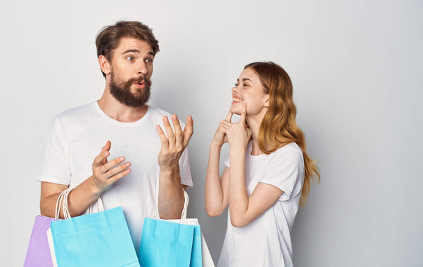 Glückliches junges Paar in weißen T-Shirts mit Paketen in der Hand Einkaufen ist Freude - Foto, Bild