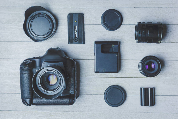 Flat lay com diferentes fotoacessórios em placas: câmera, lentes, bateria, carregador, sincronizador e tampas de lente. - Foto, Imagem