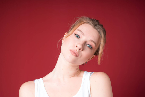 Blond woman in white tank top tilts her head on the side isolated on cherry background. - 写真・画像