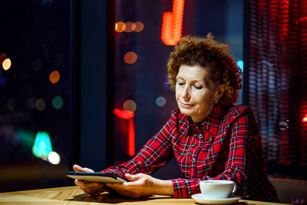 Seniorin mit Tablet in einem Café. Reife Frau entspannt sich in einem Restaurant mit Tablet-PC. Ältere Frauen nutzen digitale Tablets im Café. Technik, Alter und Menschen. Reife Studentin. - Foto, Bild