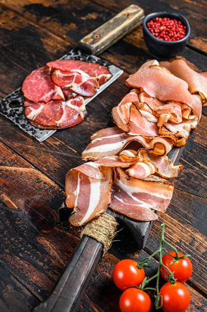 Meat antipasto board, pancetta, salami, sliced ham, sausage, prosciutto, bacon. Dark Wooden background. Top view. - Фото, изображение
