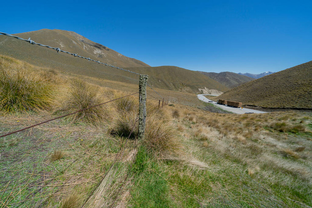 Landscape along old fence line with truck loaded with haybales on road below from lookout at top of Lindis Pass South Island New Zealand. - Photo, Image