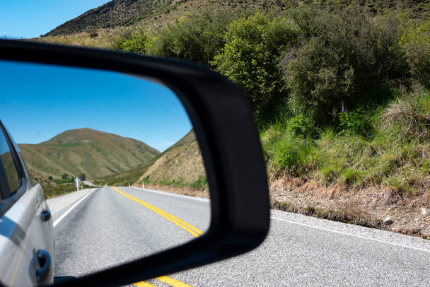 Προβολή στην εθνική οδό Lindis Pass και λόφους στο πίσω καθρέφτη της όρασης στο οδικό ταξίδι στο Νότιο νησί της Νέας Ζηλανδίας. - Φωτογραφία, εικόνα
