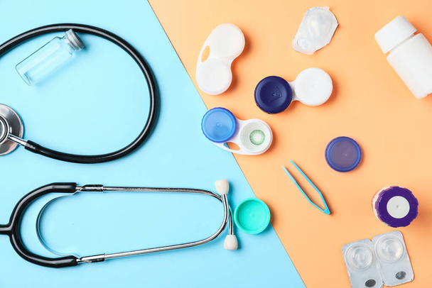 Containers with contact lenses, solutions, stethoscope and tweezers on color background - Photo, Image