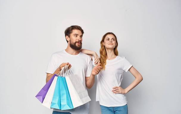 Happy young couple in white T-shirts with packages in hands Shopping is joy - Valokuva, kuva