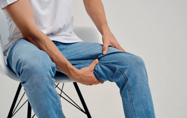 uomo in jeans seduto su una sedia e toccare la gamba con le mani ritagliato vista - Foto, immagini