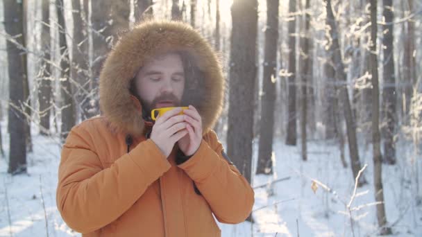 Téli turizmus és túrázás koncepció. Szakállas férfi forró itallal a téli erdőben - Felvétel, videó